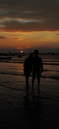 Sunset view over a calm beach with a couple enjoying the horizon.