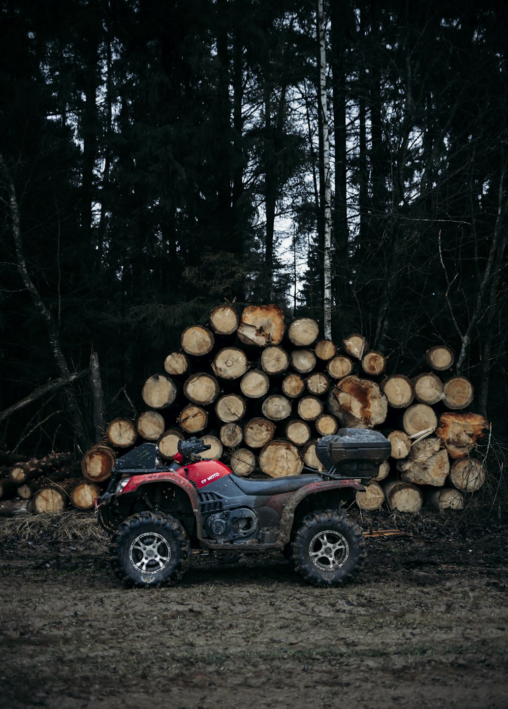 a red four wheeler parked in front of a pile of logs