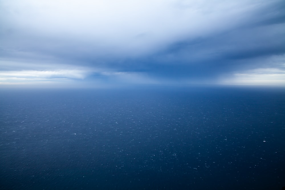 an airplane wing flying over the ocean under a cloudy sky