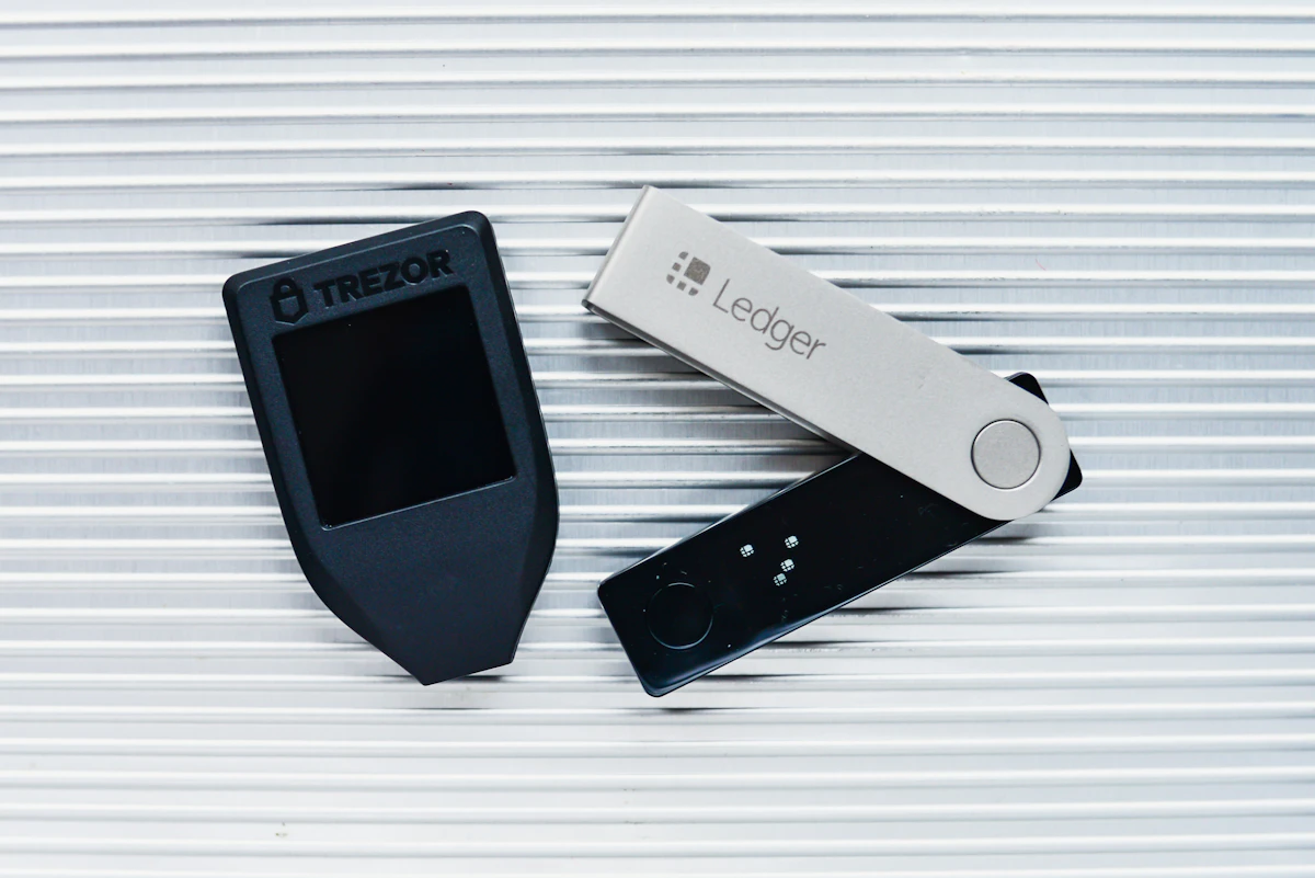 A Ledger Nano hardware wallet and a Trezor hardware wallet side by side on a ribbed metal surface