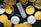 A collection of physical cryptocurrency coins scattered around a Ledger hardware wallet. The coins feature Bitcoin and Ethereum symbols, and the wallet displays a prompt to choose a PIN. The contrast between the shiny gold and silver coins and the black background creates a striking visual effect.