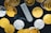 A collection of physical cryptocurrency coins scattered around a Ledger hardware wallet. The coins feature Bitcoin and Ethereum symbols, and the wallet displays a prompt to choose a PIN. The contrast between the shiny gold and silver coins and the black background creates a striking visual effect.