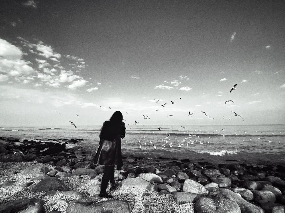 a woman standing on a rocky beach next to the ocean