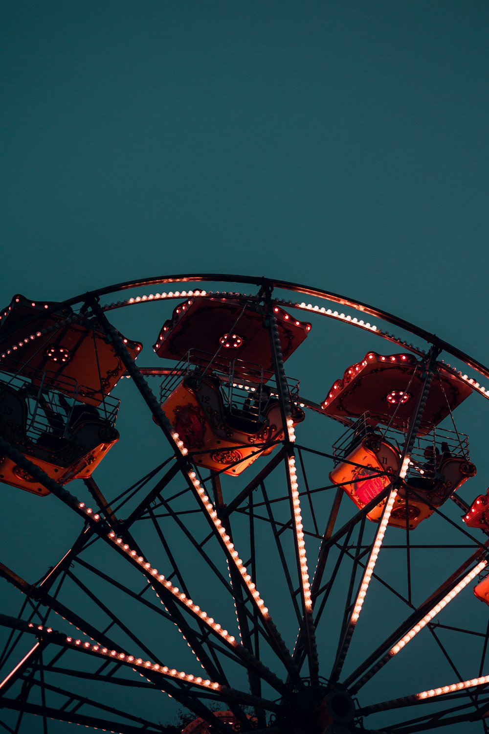 a ferris wheel lit up at night with the moon in the background