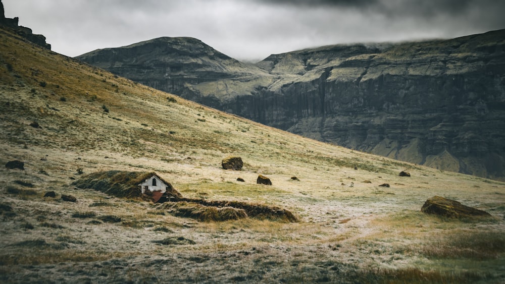 a small house on a grassy hill with mountains in the background