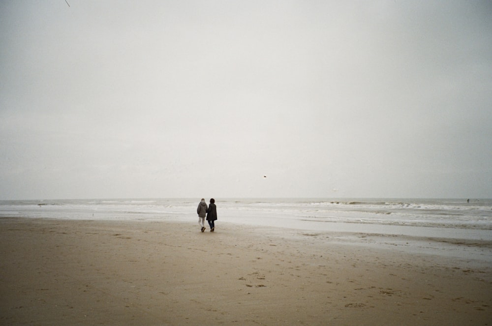 two people walking on a beach with a kite in the sky