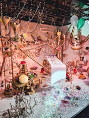 An intricate, whimsical scene filled with metallic steampunk elements, including gears, pipes, and funnels. Various colorful decorations and sparkling gems are scattered throughout. There are also brightly colored objects like balloons and confections, creating a festive atmosphere.
