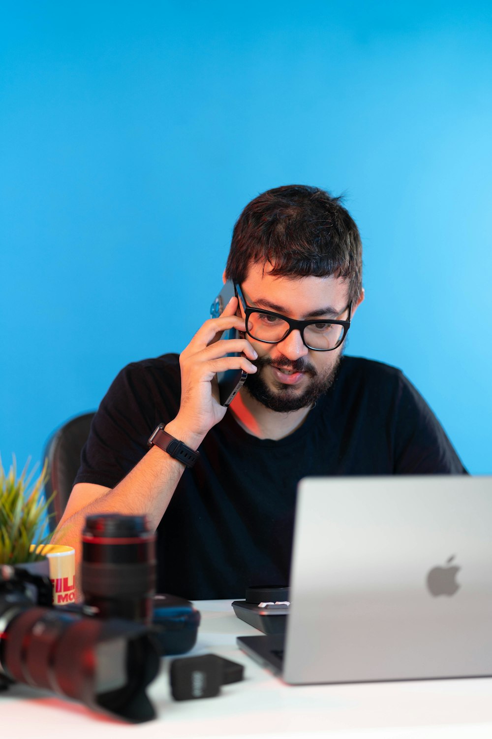 a man sitting in front of a laptop talking on a cell phone