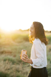 A cheerful farmer holding a bottle of fresh Jeje Segar milk in a sunny green pasture.