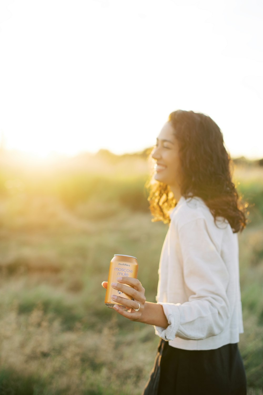 a woman standing in a field holding a can