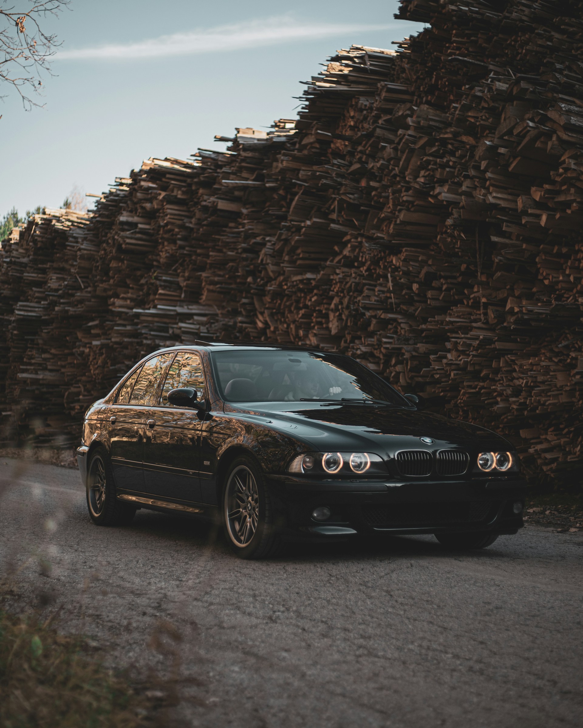 a black car parked in front of a pile of logs