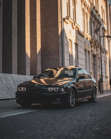 Sleek black luxury sedan with gold accents parked in front of a historic Fes building at sunset.