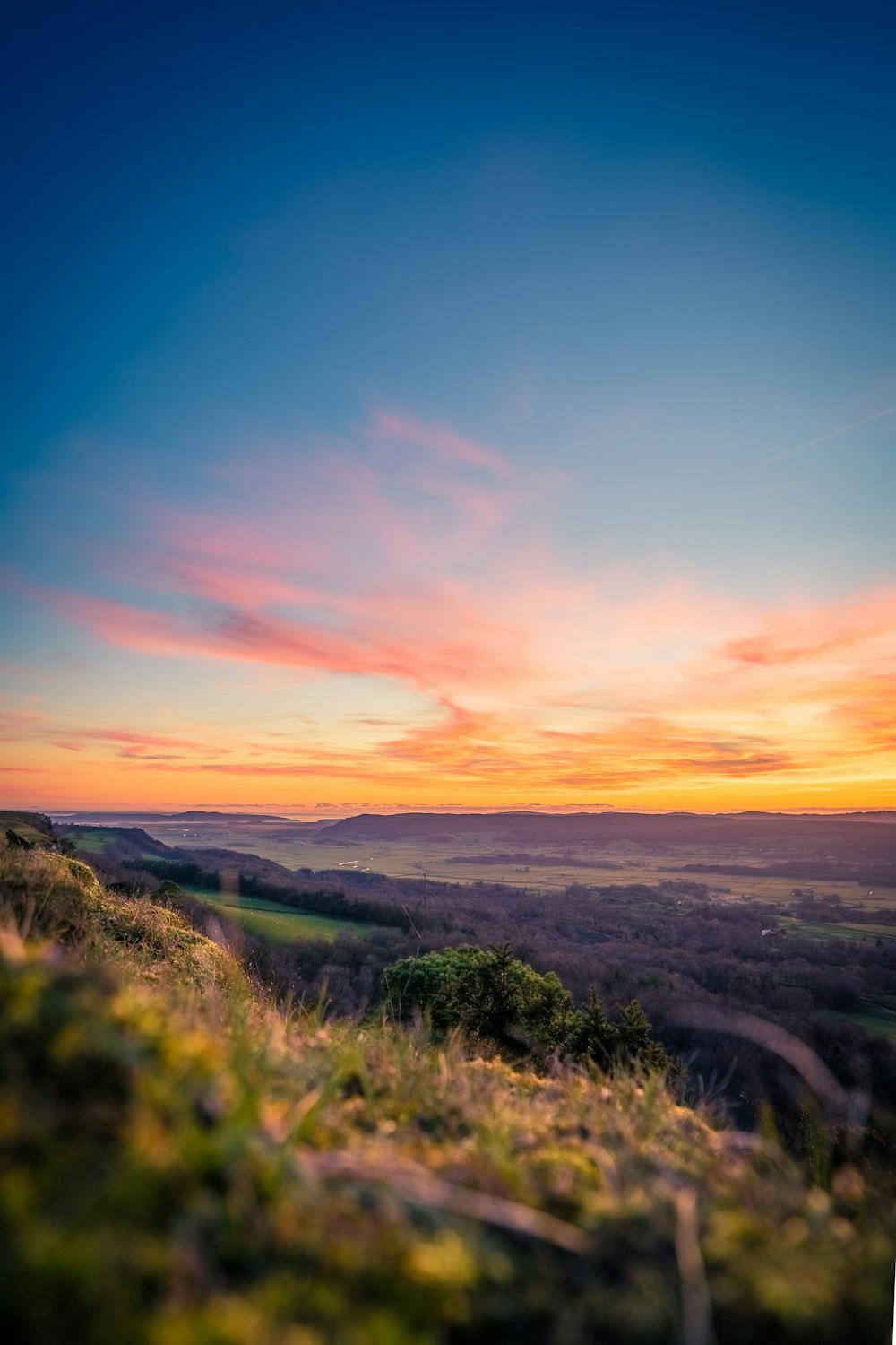 the sun is setting over a grassy hill