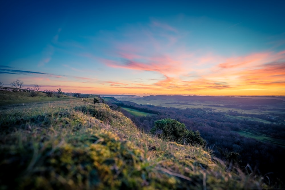 the sun is setting over a grassy hill