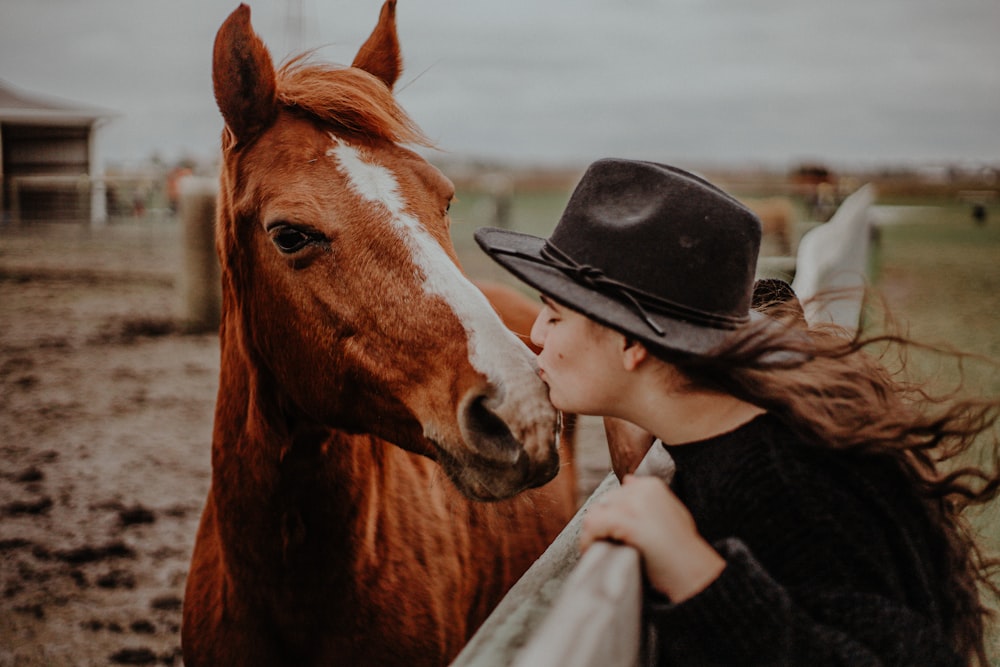 Una mujer con sombrero está acariciando a un caballo