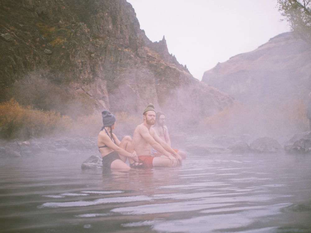 three people sitting in a body of water