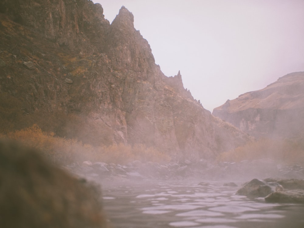 a foggy river with rocks and a mountain in the background