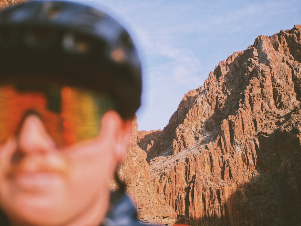 a man wearing a helmet and goggles standing in front of a mountain