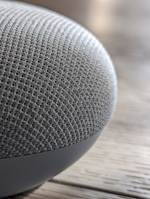 A close-up view of a textured fabric surface on a rounded electronic device, resting on a wooden surface.