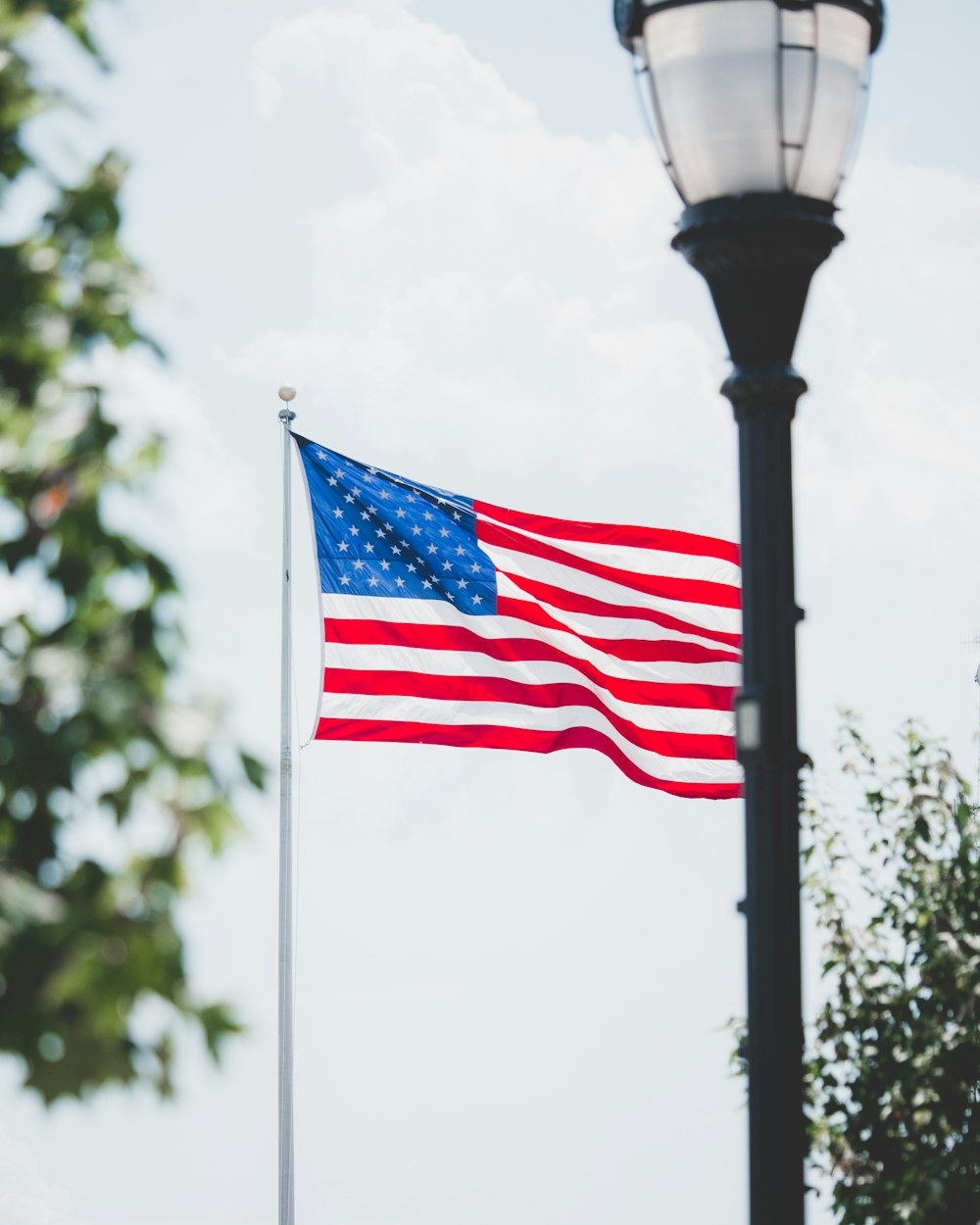 an american flag flying in the wind next to a lamp post