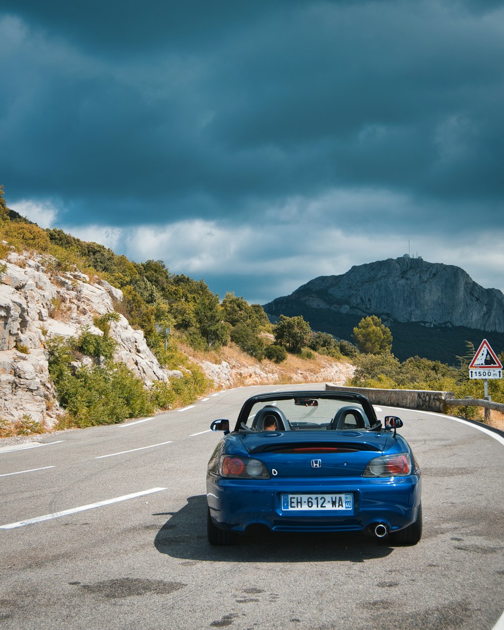 a blue convertible car driving down a winding road
