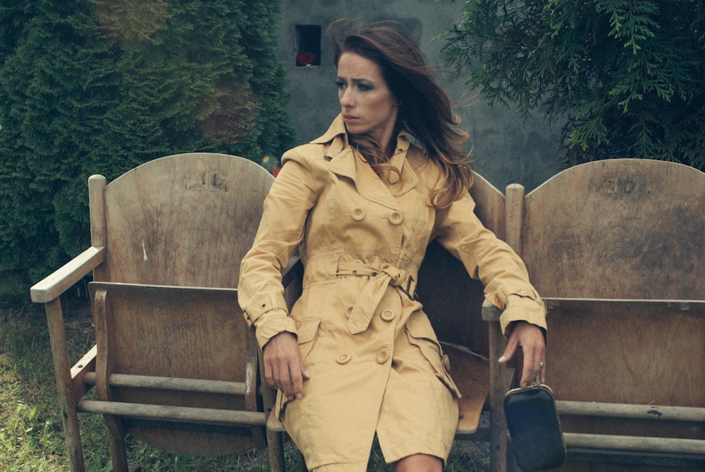 a woman in a trench coat sitting on a bench