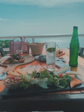 A vibrant Mediterranean table set outdoors with fresh vegetables, olive oil, and colorful dishes under warm sunlight.