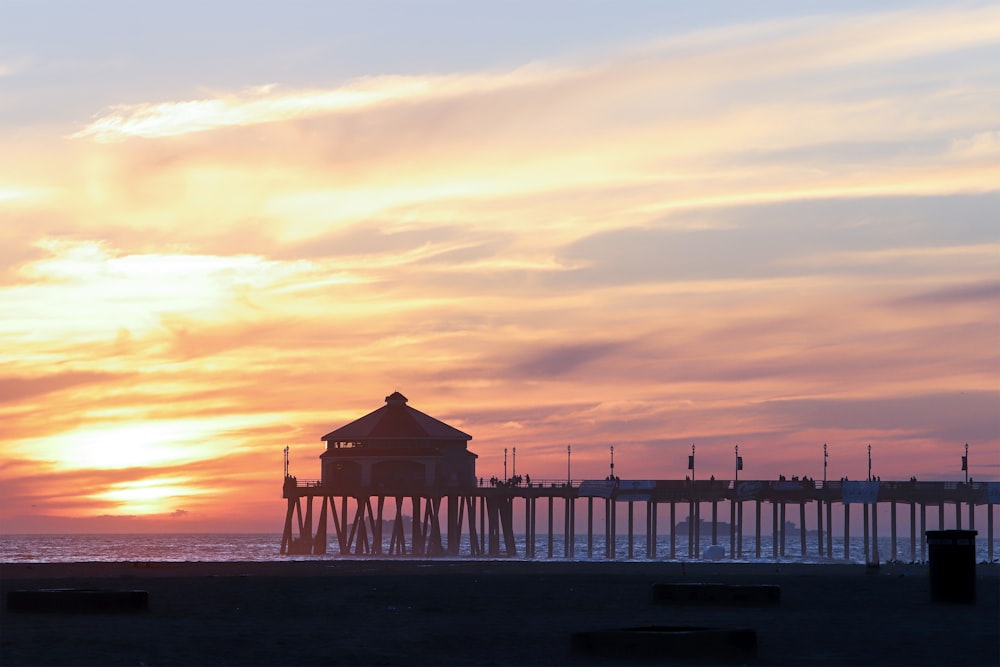 the sun is setting over the ocean with a pier in the background