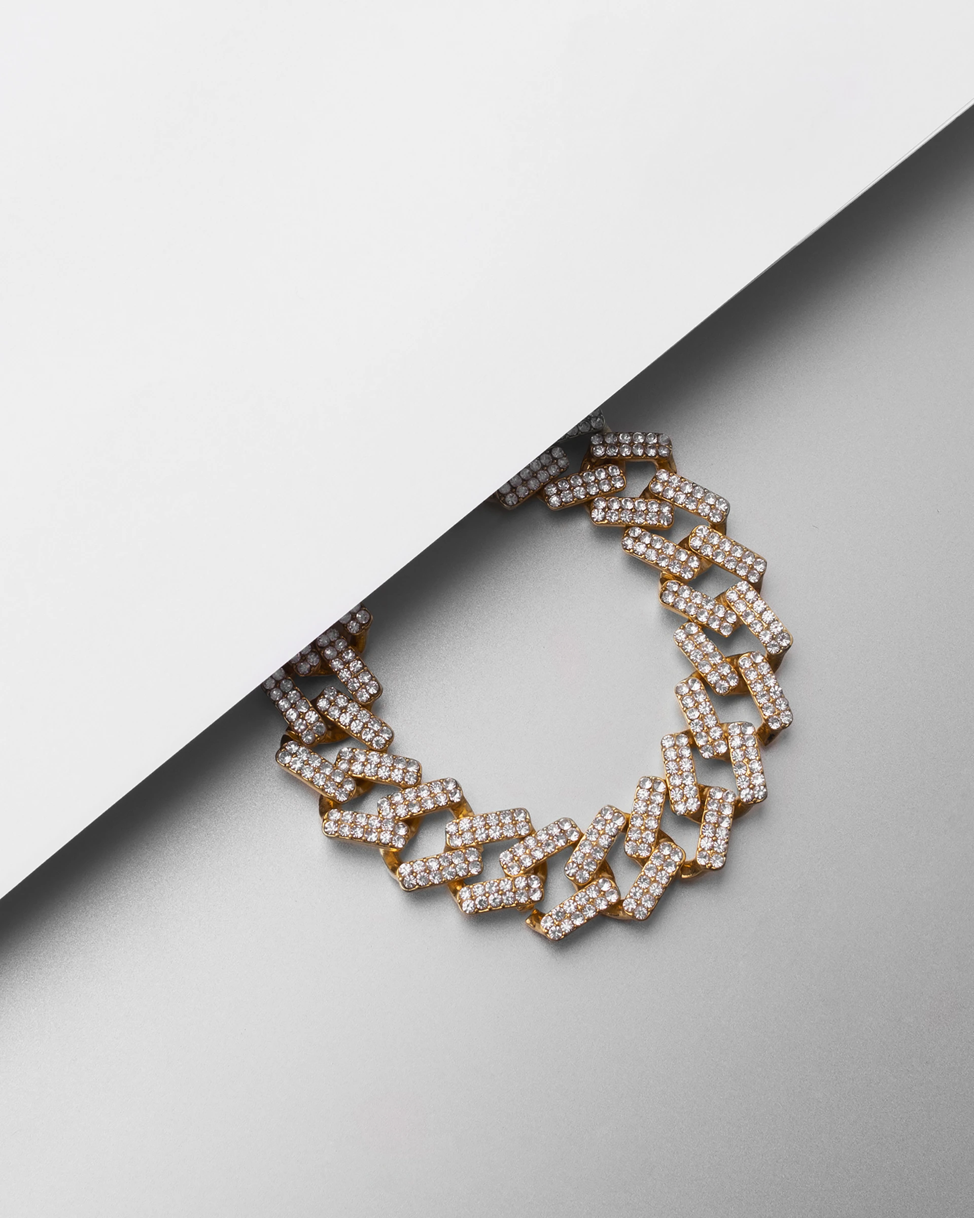 Close-up of a stylish gold necklace with intricate modern design, resting on a pearl white fabric background.