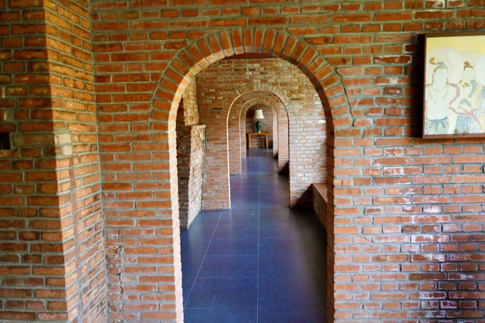 a long brick hallway with a painting on the wall