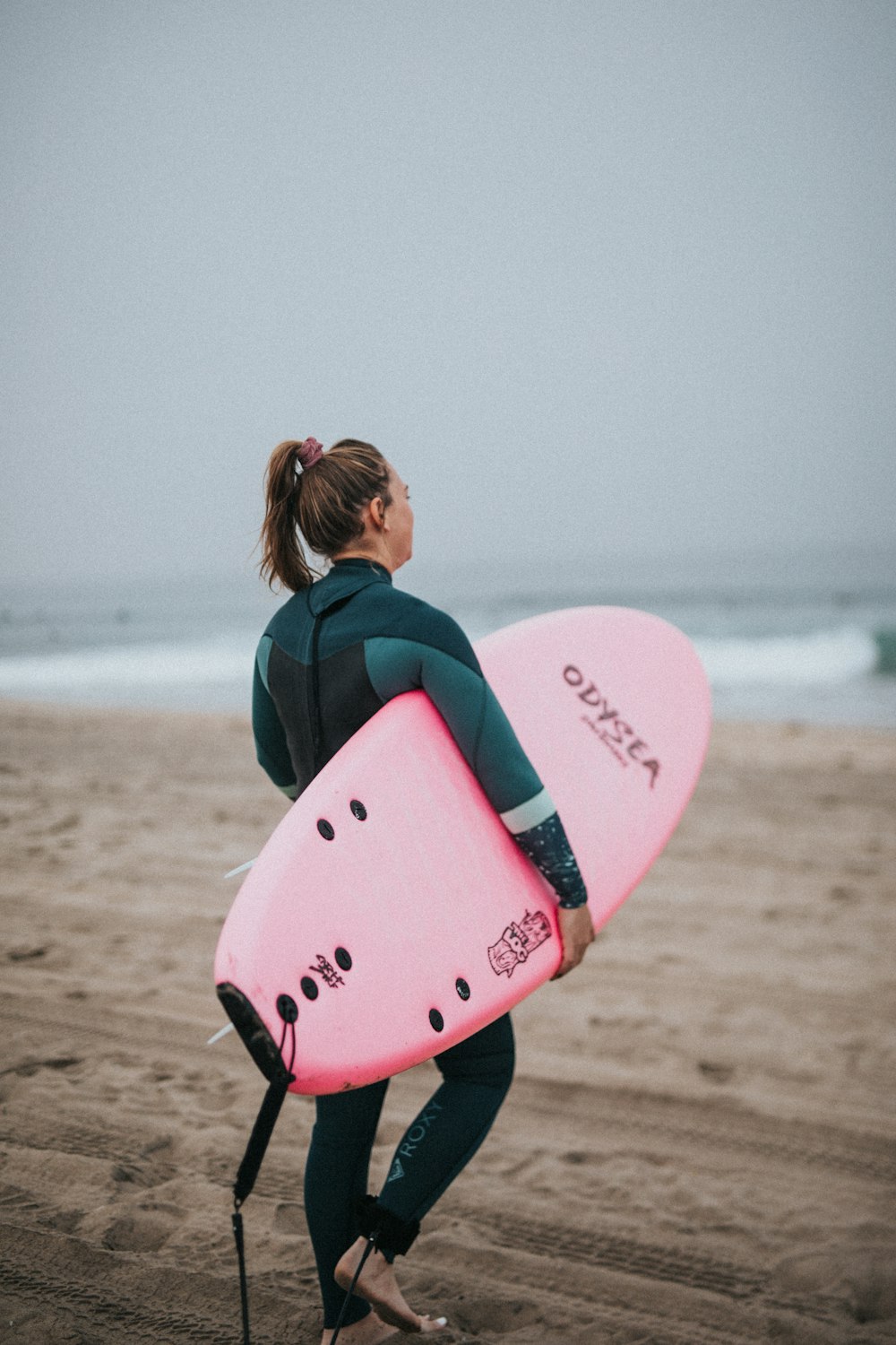 uma mulher em um traje de mergulho carregando uma prancha de surf rosa