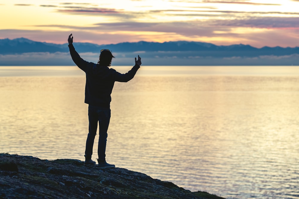 a man standing on top of a hill next to a body of water