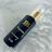 A sleek black bottle with gold detailing, labeled 'HB Improve' and 'Stem cells hair serum', placed on a marble surface. The bottle has a clear cap and a gold pump.