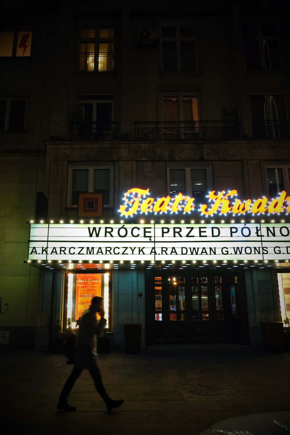 a person walking past a theater marquee at night