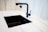 A modern kitchen sink setup with a matte black faucet and a matching black rectangular sink set in a white marble countertop. The faucet has a minimalist design with a sleek handle. The surrounding area shows clean, white, marble-like surface creating a contemporary and elegant look.