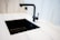 A modern kitchen sink setup with a matte black faucet and a matching black rectangular sink set in a white marble countertop. The faucet has a minimalist design with a sleek handle. The surrounding area shows clean, white, marble-like surface creating a contemporary and elegant look.