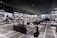 A modern sneaker store with sleek black shelving displaying various athletic shoes and sports apparel. Central seating areas and spotlights provide a contemporary retail ambiance. The signage prominently features a famous sportswear slogan in the background.