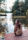 a woman sitting on a bench in front of a lake