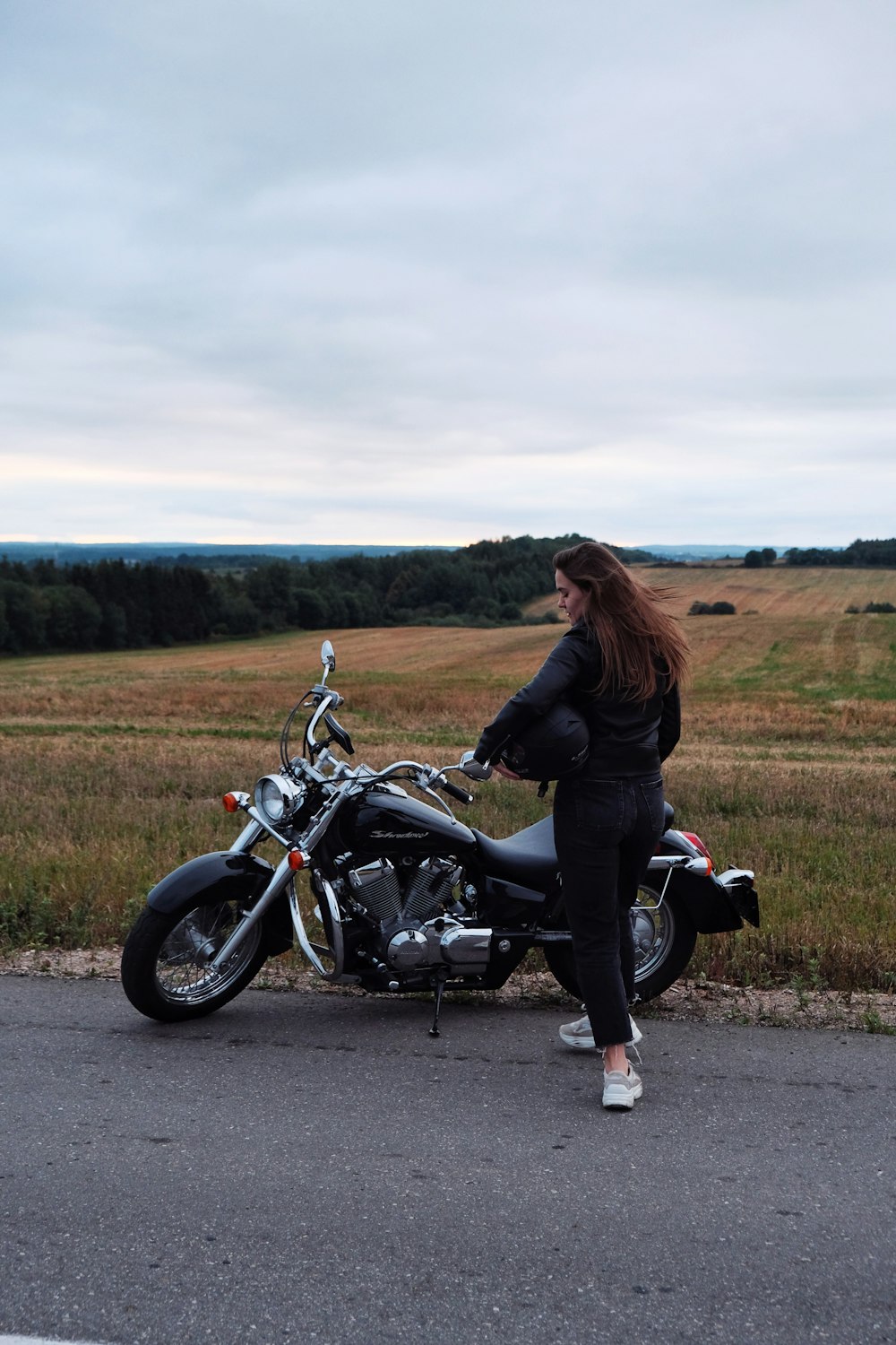 a woman standing next to a motorcycle on a road