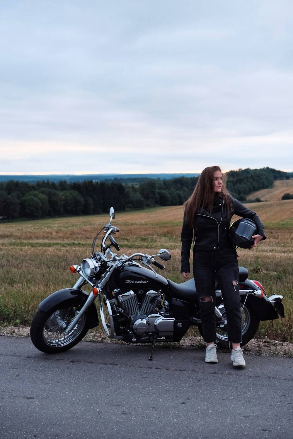 a woman standing next to a motorcycle on a road