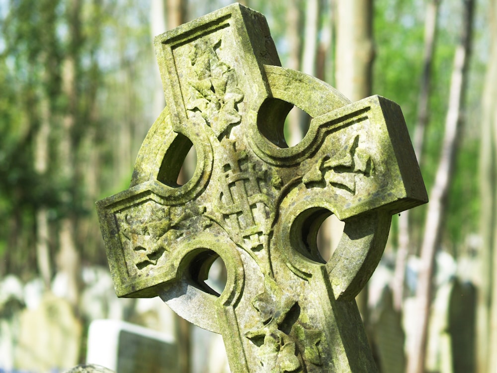 Una croce di pietra in un cimitero con alberi sullo sfondo