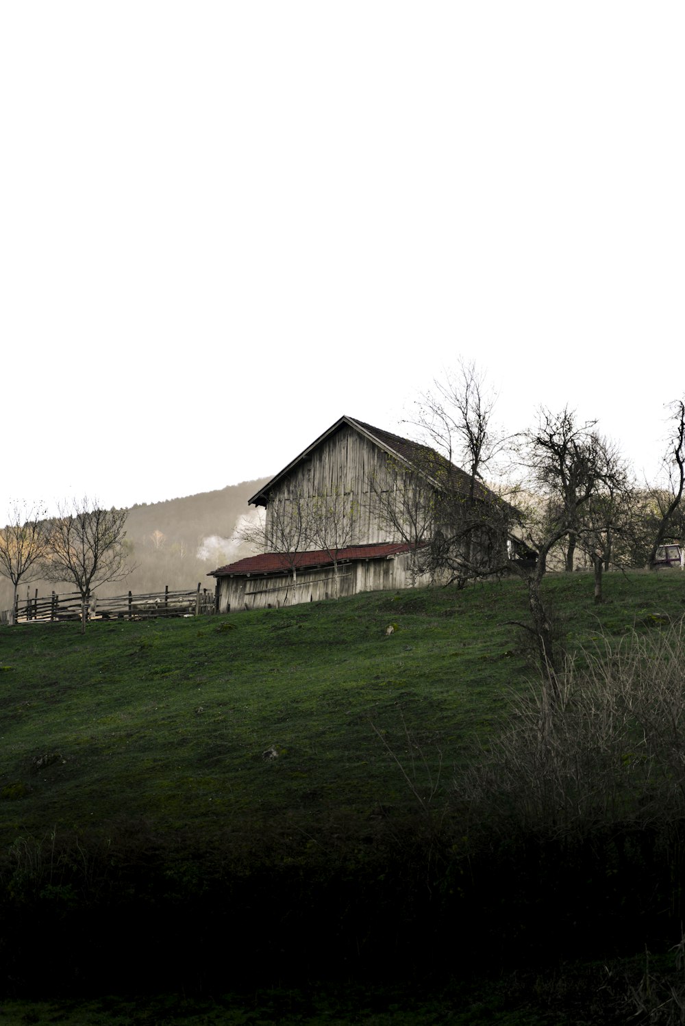 a barn on a hill with trees in the foreground