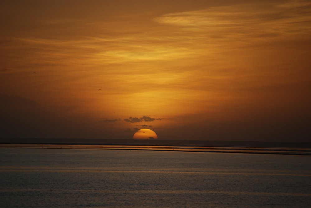 the sun is setting over the ocean on a cloudy day