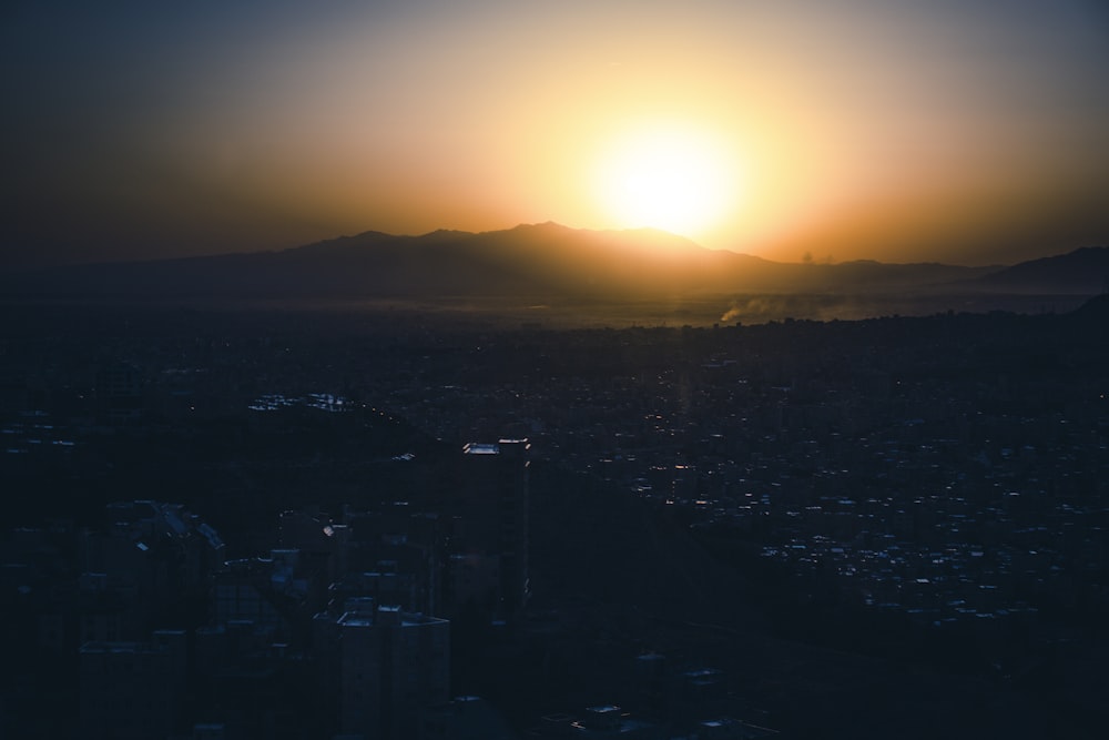 the sun is setting over a city with mountains in the background