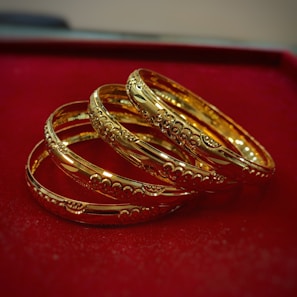 Stacked gold bangles resting on a polished charcoal stone surface, highlighting their smooth shine.