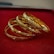 A set of intricately designed gold bangles with detailed patterns is placed on a plush red surface. The bangles exhibit a polished, reflective finish, enhancing their luxurious appearance.