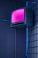 A vintage television with a pink glowing screen is mounted on a tiled wall with ambient blue lighting. The scene has a retro-futuristic aesthetic with its contrasting neon colors.