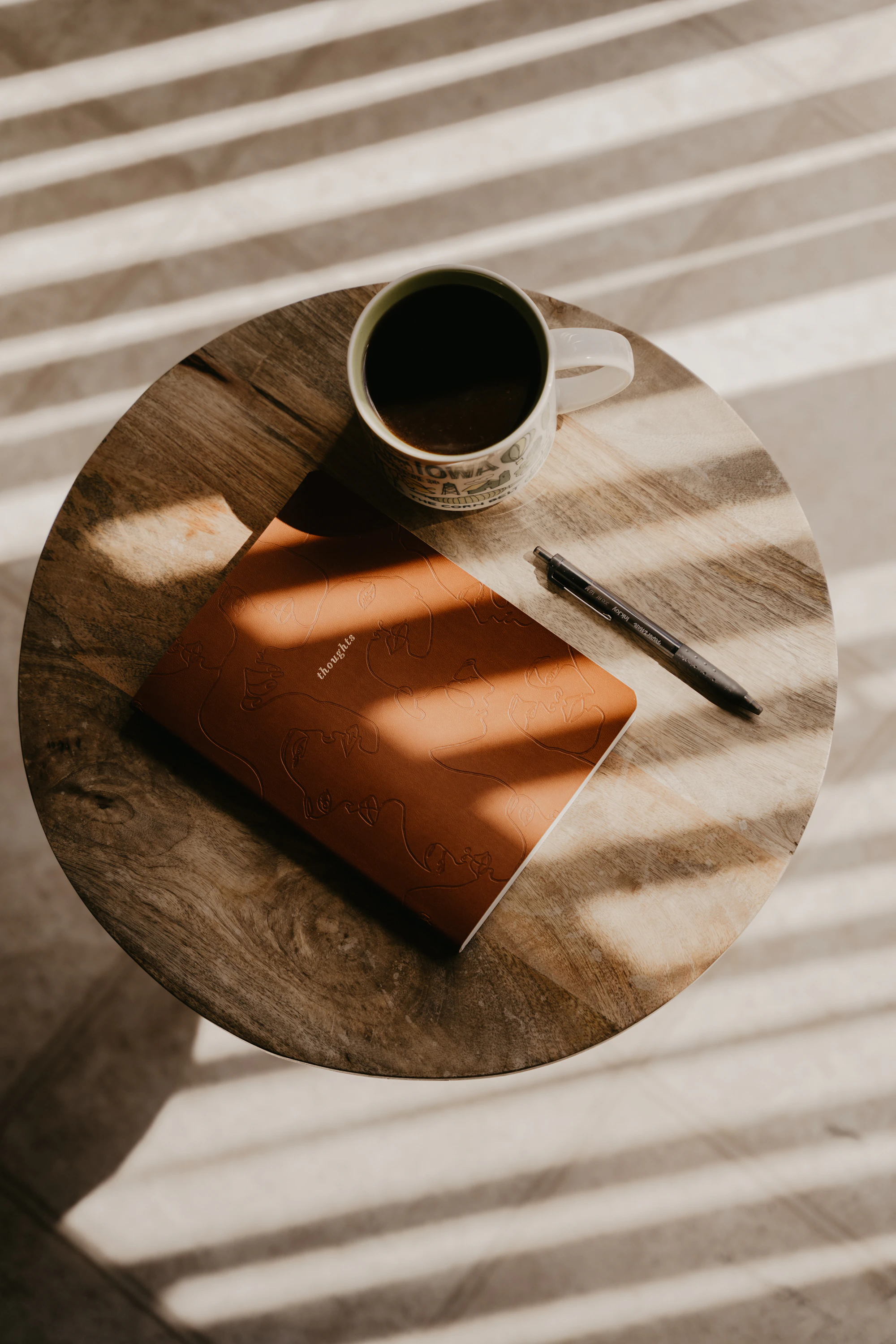 A coffee cup and notebook resting in warm sunlight on a wooden table