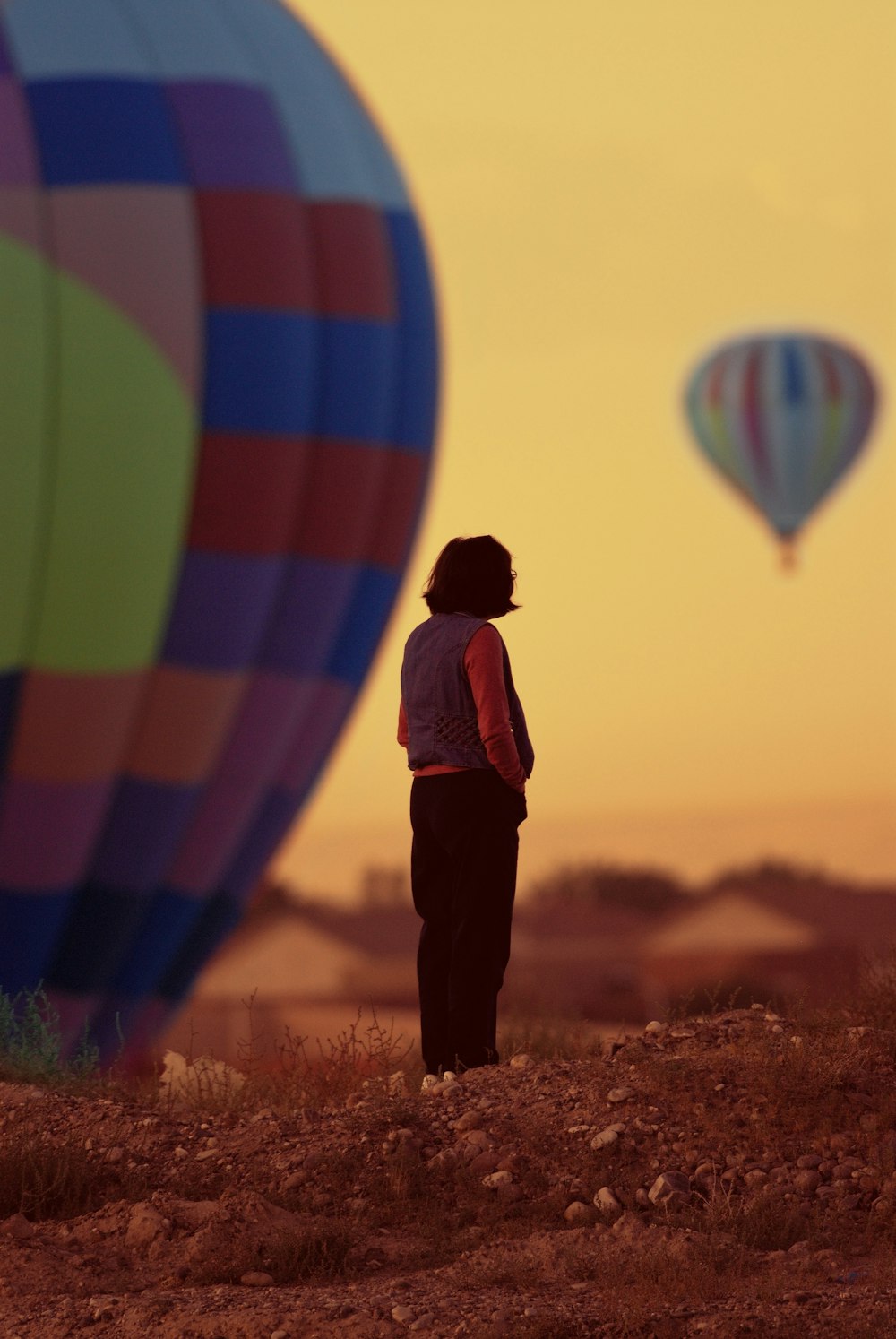 a person standing in a field watching hot air balloons