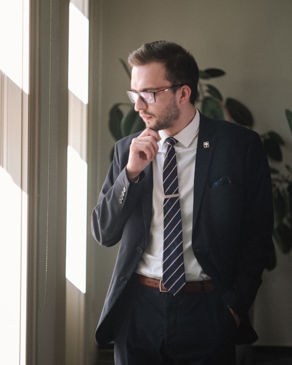a man in a suit and tie standing in front of a window